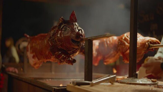 Roasted a whole big pig on fire. Grilled on a big skewer. Roasting piglet on a spit turns slowly roasting it. Barbecue. Street food. 4k. Lechon or Suckling popular dish. pigs roasting on fire pit and 