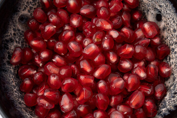 Gennevilliers, France - 01 02 2024: Close up of a gray and white clay bowl filled with red triangular pomegranate seeds on a white background.