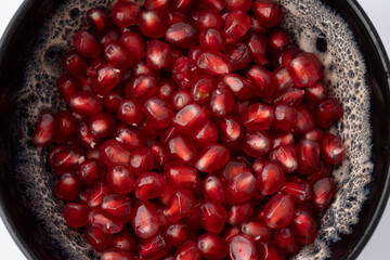 Gennevilliers, France - 01 02 2024: Close up of a gray and white clay bowl filled with red triangular pomegranate seeds on a white background.