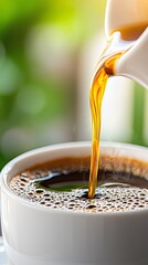 A cup of coffee being poured into a white cup