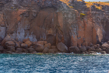 A rocky cliff and the blue calm sea water. Grotta del Cavallo Vulcano, the tourist attraction. Volcanic stone coastline in the clear waters of the Vulcano island located in the near Piscina si Venere