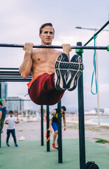 Strong Caucasian male athlete training torso and biceps using bars at sports playground during...