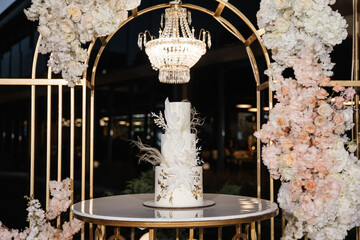 Trendy wedding cake against the backdrop of an expensive luxury wedding arch with fresh flowers and...