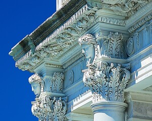 Ornate white architectural detail with female busts against a blue sky.