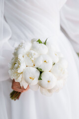 Portrait of a bride in a luxurious dress and with a bouquet of white peonies in her hands. Close-up photo