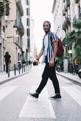 Cheerful ethnic man crossing road in old town