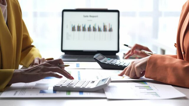 Two women are working on a spreadsheet together. One of them is pointing at a number on the screen