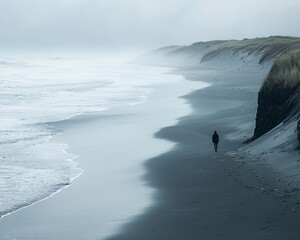 Solitary figure walking along a misty, dark sand beach with ocean waves.