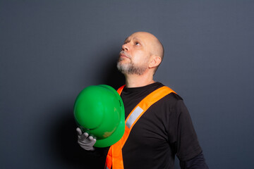 Photo of a civil worker in gloves and reflective vest holding green helmet against his chest....