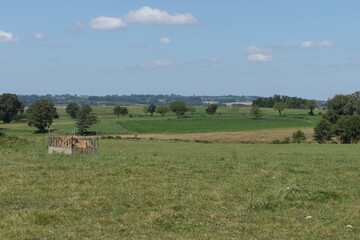 From a hilltop, a breathtaking panoramic view unfolds over the green patchwork of French agricultural fields. Rolling hills stretch into the horizon.