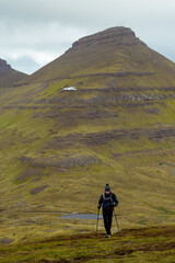 Hiker with poles in a Dramatic landscape from dangerous and beatiful Faroe Islands with a helicopter in the background