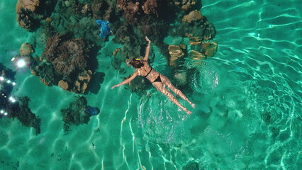 Young woman swimming in turquoise crystal clear water above colorful coral reef wearing snorkeling mask and black bikini during summer vacation in tropical destination