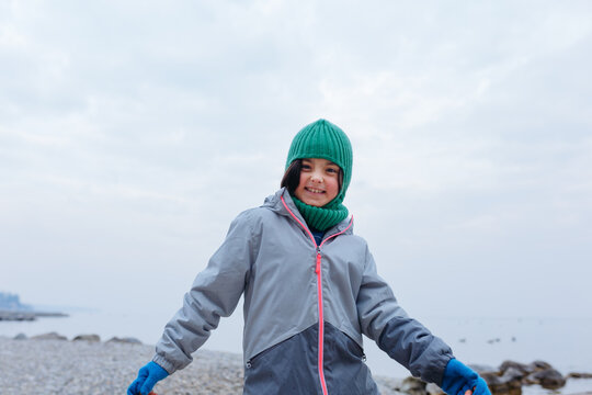 portrait of smiling girl in green winter hat standing in front of the lake