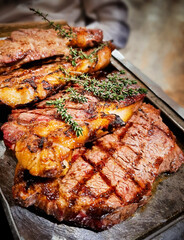 Closeup view of four slices of cooked grilled juicy strip steak, also porterhouse or sirloin, made of beef meat loin, seasoned with fresh herbs served on frying pan prepared for eating at restaurant