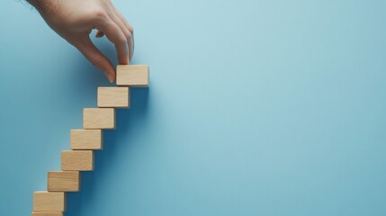 A hand arranging wooden blocks into a staircase formation on a blue background.