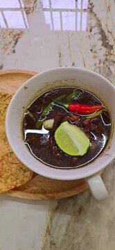 Rawon soup or Indonesian black beef soup, black color are from indonesian nut called kluwek. Served with lime, chili paste, salted egg, and tempe cracker
