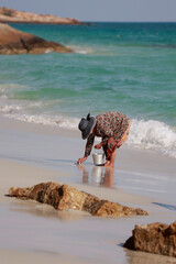 an elderly woman collects shellfish on the coast