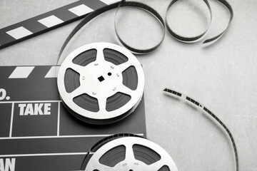 Movie clapper and film reels on grey textured table, closeup