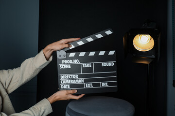 Woman with clapperboard near spotlight on black background, closeup