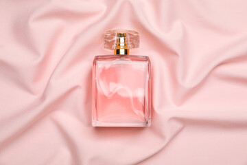 Bottle of perfume on pink silk fabric, top view