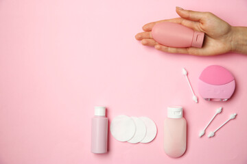 Woman holding cream near other skin care products on pink background, top view