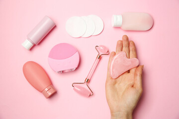Woman holding gua sha tool near other skin care products on pink background, top view