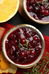Tasty cranberry sauce in bowls, orange, thyme and cinnamon on black table, top view