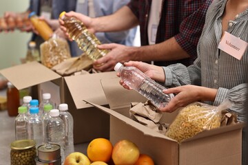 Group of volunteers packing food donations at table indoors, closeup