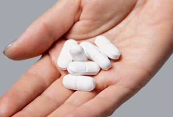 Cupped womans hand with a pile of mixed white medical pills closeup over grey