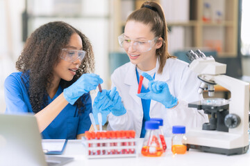 Two beautiful female doctors sitting at a table in a science lab with test flasks. Colorful glass...
