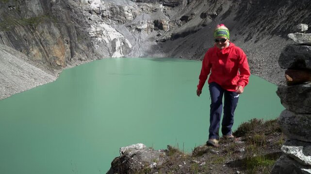 Smiling Female trekker dressed bright red jacket acclimatization round walking along high altitude Sabai Tso glacial lake cca 4350m. Makalu Barun National Park, Mera peak climbing route, Nepal