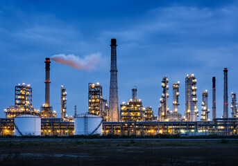 Industrial oil refinery plant emitting smoke at twilight with blue sky