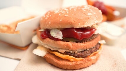 Double patty cheeseburger with lettuce, ketchup, pickles and cheese in a sesame seed bun on a napkin against the background of fast food packaging.