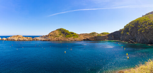 Fototapeta premium Panorámica de Cala Ses Vaques con aguas azules, colinas rocosas y cielo despejado, Costa Brava, España.