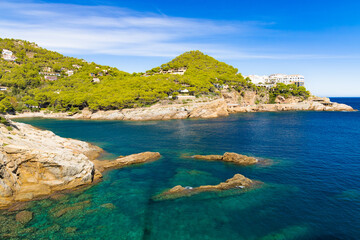 Fototapeta premium Cala d'Aiguafreda con aguas cristalinas, rocas y pinos, rodeada de colinas verdes, Costa Brava, España.