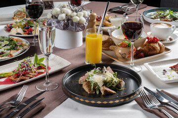 A festive table with a variety of entrees, pizza, porridge, steaks, desserts.