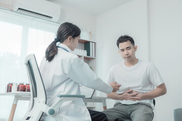 Obraz premium Asian man suffers from abdominal pain, ulcerative colitis. Doctor with computer tablet consulting male patient with abdominal pain in hospital examination room health technology