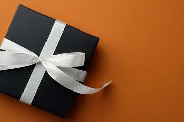 Beautiful gift box with bow on orange background, top view. Space for text