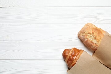 Paper bag with fresh baguette and croissant on white wooden table, top view. Space for text