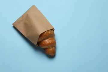 Paper bag with fresh croissant on light blue background, top view. Space for text