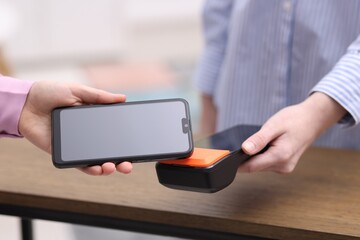Woman paying with smartphone via terminal at wooden counter indoors, closeup