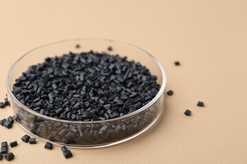 Black plastic granules in petri dish on beige background, closeup. Space for text