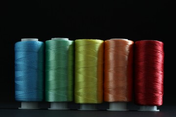 Spools of colorful sewing threads on black background