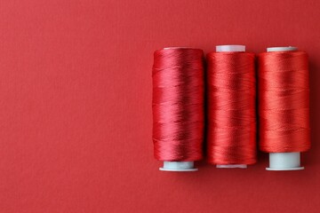 Spools of colorful sewing threads on red background, flat lay. Space for text