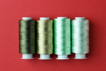 Spools of colorful sewing threads on red background, flat lay