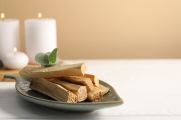 Palo santo sticks and eucalyptus leaves on white wooden table, closeup. Space for text