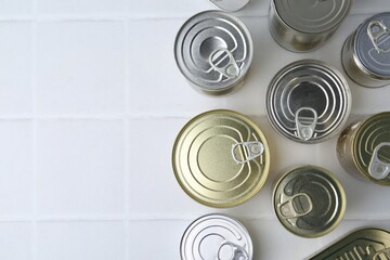 Many closed tin cans on white tiled table, flat lay. Space for text