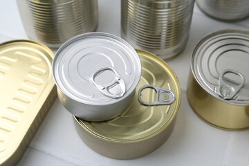 Many closed tin cans on white tiled table, closeup