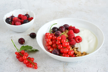 a bowl of berries and yogurt sits next to a bowl of raspberries