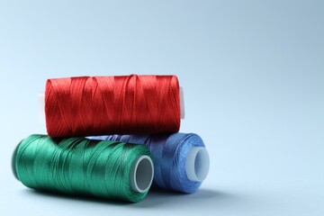 Spools of colorful sewing threads on light background, closeup. Space for text